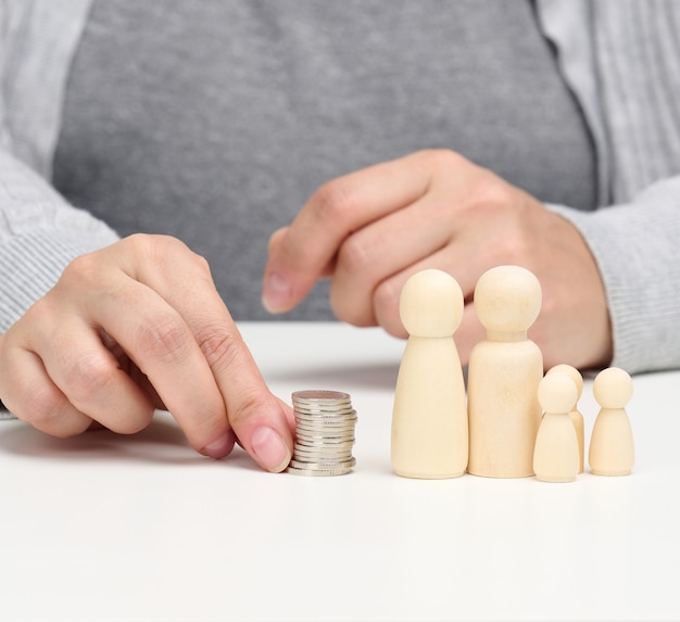 Hand puts coins in a pile and wooden figurines of a family on a white table. Economy and investment concept, budget planning. Receiving subsidies from the state, tax