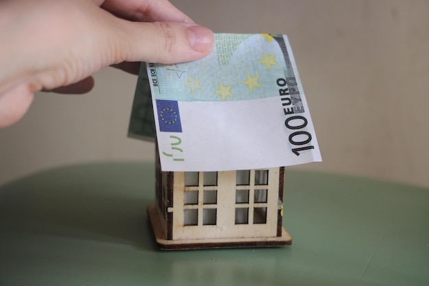 Hand puts Euro bill like roof on toy house Buying property RE business concept