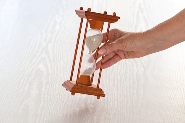 Hand puts hourglass on white wooden table