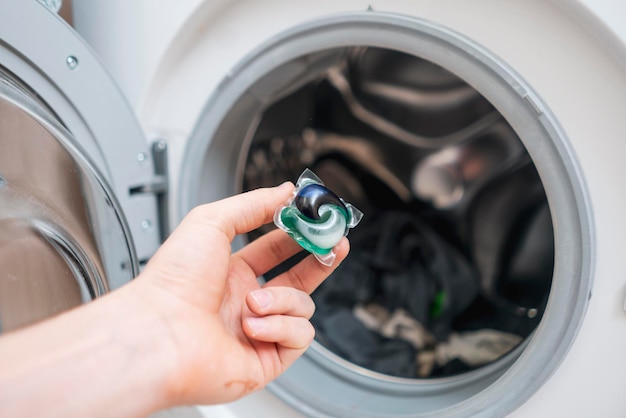 A hand puts laundry powder capsule in washing machine with
colorful clothes