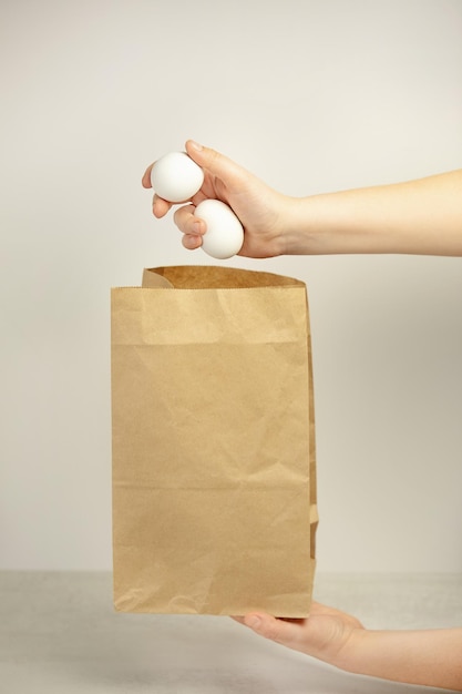 A hand puts white eggs in a packet on a white background