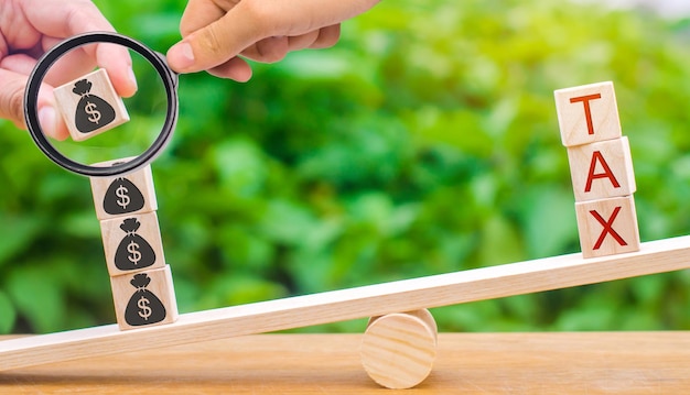 A hand puts wooden blocks with dollars on scales and the word tax