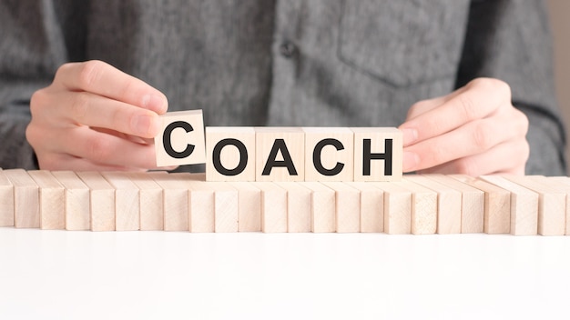 The hand puts a wooden cube with the letter C from the word COACH.