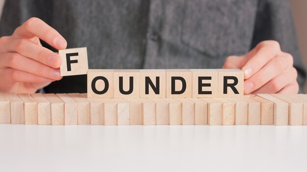 The hand puts a wooden cube with the letter P from the word FOUNDER