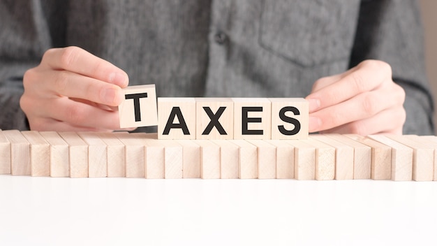 The hand puts a wooden cube with the letter t from the word taxes.
