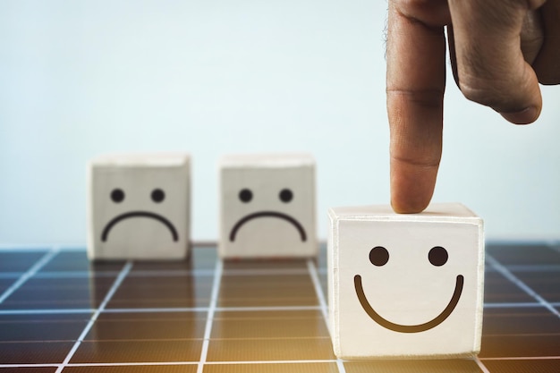 La mano mette i cubetti di legno con la faccia sorridente nel lato luminoso e la faccia triste al buio sul pannello solare fotovoltaico mentalità positiva concetto di energia pulita