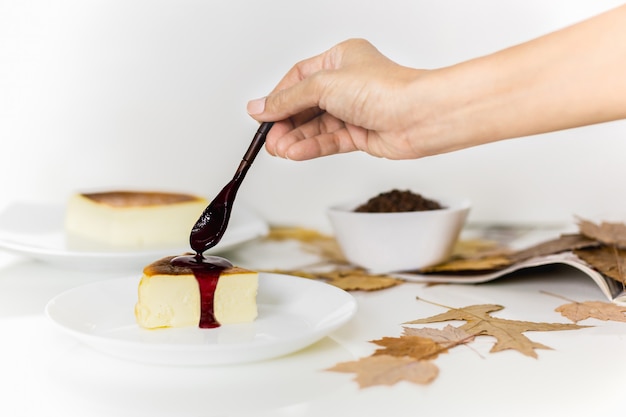 Photo hand putting berry sauce with wooden spoon on cheesecake.