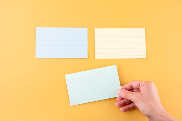 Hand putting blank writing paper and two empty papers on a yellow background space for text