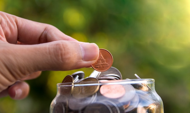 Photo hand putting a coin in a jar