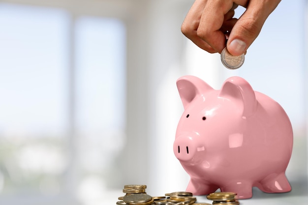 Hand putting coin to piggy bank and coins on bokeh background