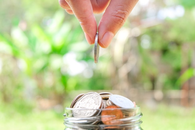 Foto mano che mette le monete nel barattolo di vetro. risparmiare e investire denaro per prepararsi in futuro.