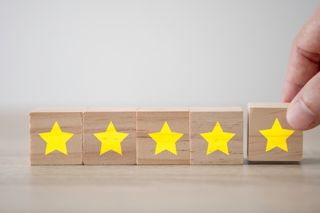 Hand putting five yellow stars which printed screen on wooden cube. Customer experience survey and satisfaction feedback concept.