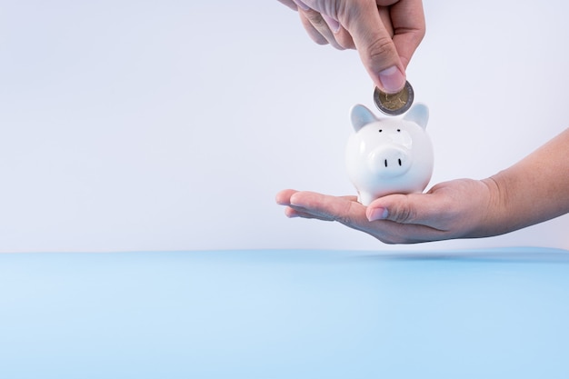 Hand putting money coin into piggy bank isolated grey background. Property investment and house mortgage financial concept.