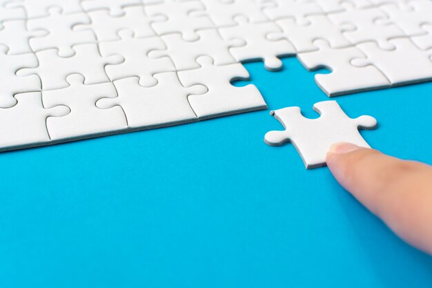 Hand putting piece of white jigsaw puzzle on blue background