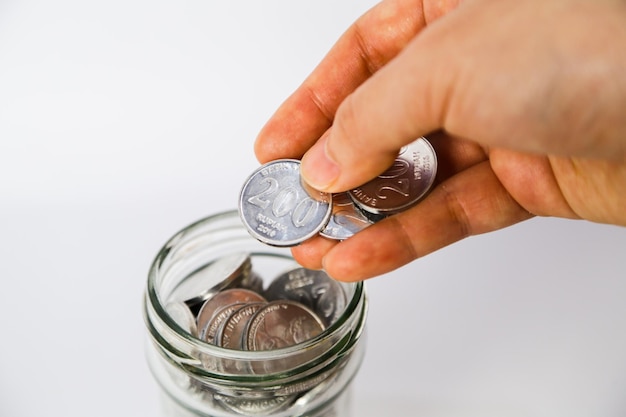 A hand putting three Indonesian silver coins in a glass of jar close up