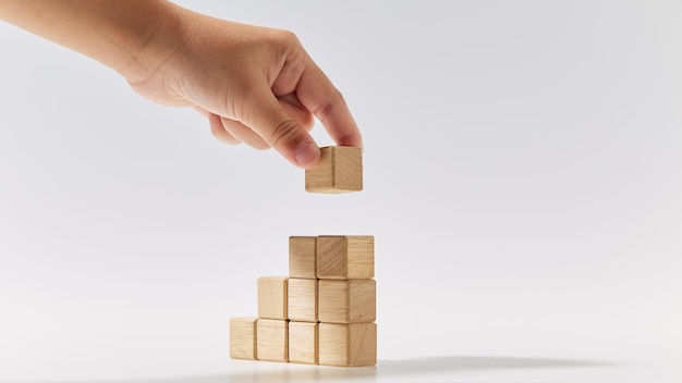 Hand putting wood cubes stacked as stair step shapes on white