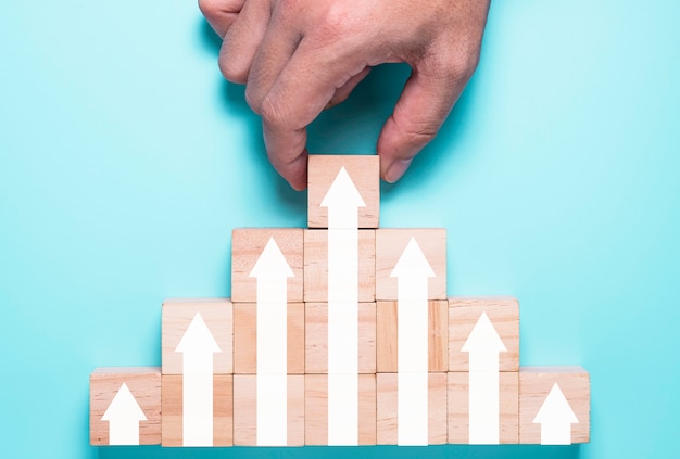 Hand putting wooden cubes block which print screen increase or up white arrow. It is symbol of economic investment profit growth.