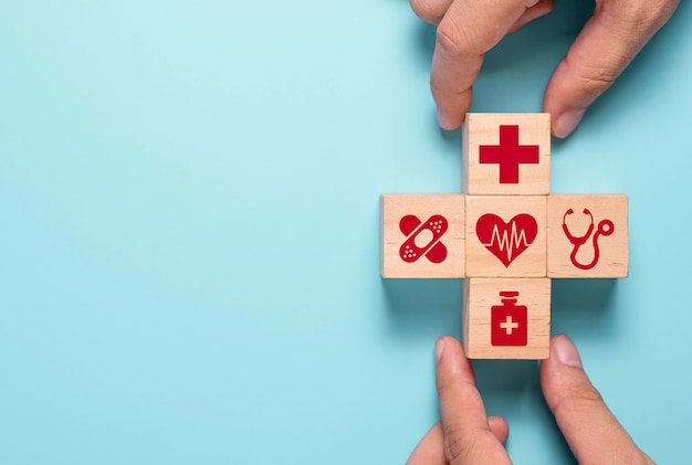 Hand putting wooden cubes of healthcare medicine and hospital icon on blue table. Health care insurance business and investment.