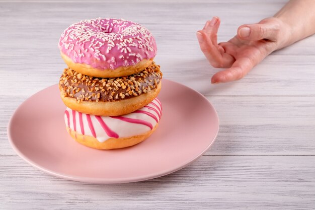 A hand reaches out for three pink donuts