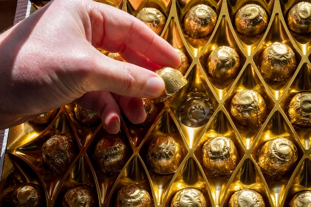 Hand reaching for chocolate in golden wrap closeup view