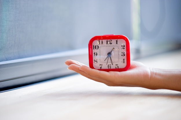 Hand and red alarm clock that shows the alarm at all Every morning