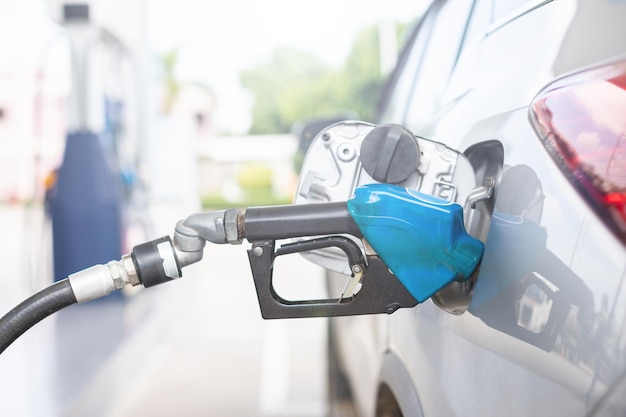 Hand of refueling worker are filling fuel to car in Petrol station Focus on fuel nozzle and blur day light background