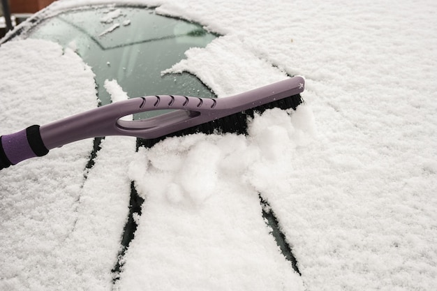 hand removing snow from car with a brush