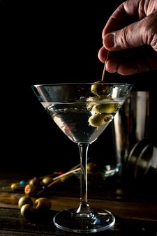 Una mano che rimuove alcune olive da un classico bicchiere da martini conico e genera schizzi. orientamento verticale.
