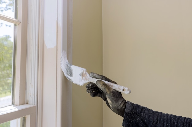 Photo hand of repairman painting with gloves in the painting window molding trim