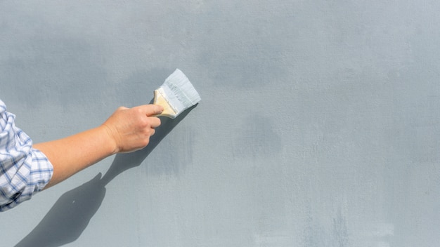 絵筆を持った修理工の手が壁を青く塗ります。