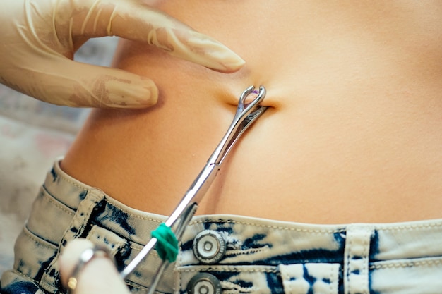 Photo hand in a rubber glove close-up of master prepares to pierce the navel by belly of a young woman with a bandage and cotton on her stomach. care navel ring piercing concept