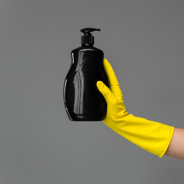 A hand in a rubber glove holds a bottle of dishwashing detergent 