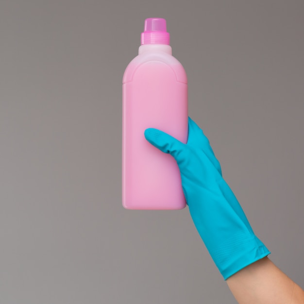 A hand in a rubber glove holds a bottle of plumbing detergent 