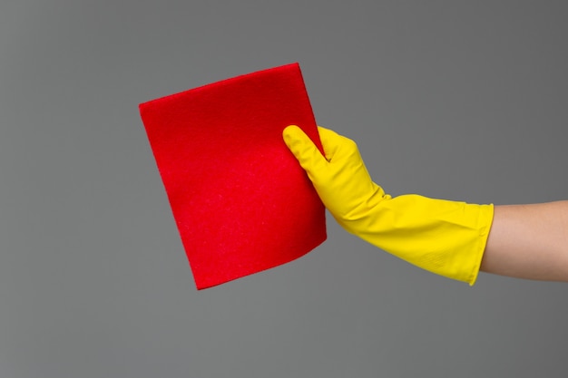 A hand in a rubber glove holds a bright microfiber duster on a neutral background