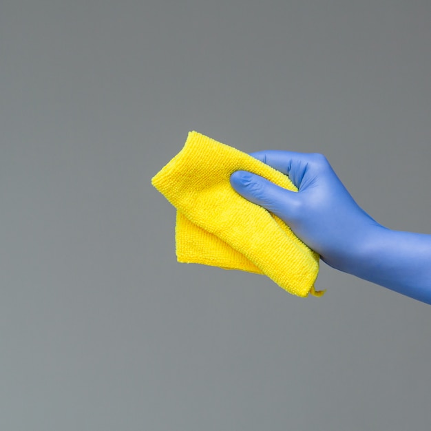 A hand in a rubber glove holds a bright microfiber duster