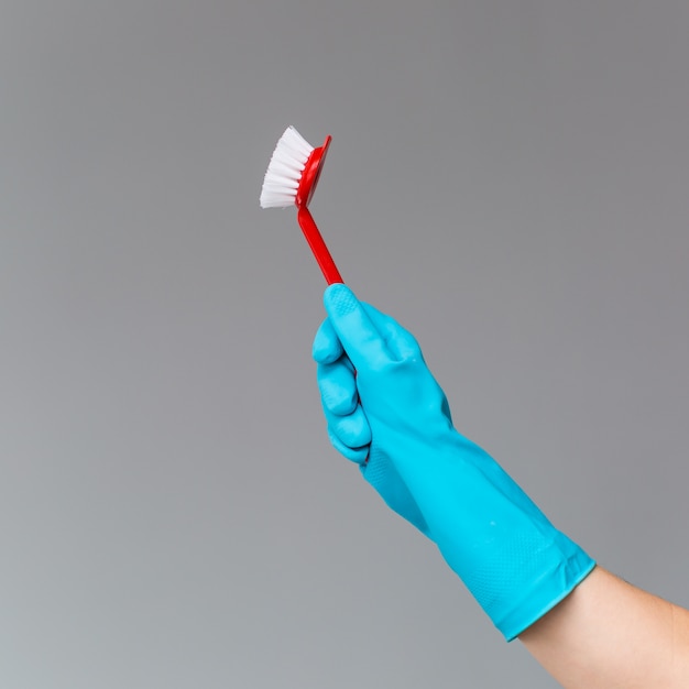 A hand in a rubber glove holds the dishwashing brush 