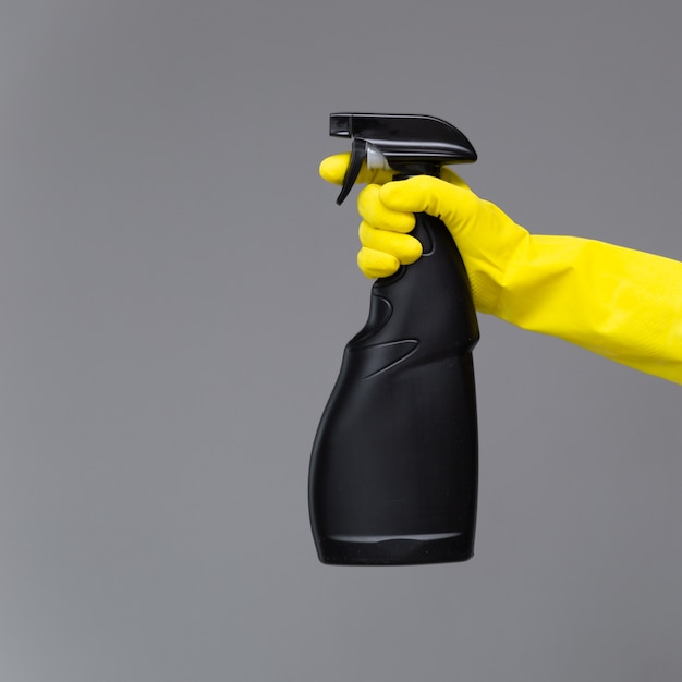 A hand in a rubber glove holds the glass cleaner in a spray bottle