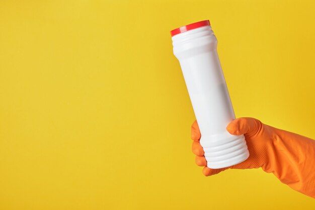 Hand in a rubber glove holds a jar of cleaning powder on a yellow background