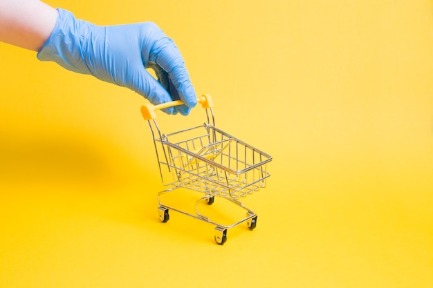 Hand in rubber glove holds a miniature shopping trolley by the handle