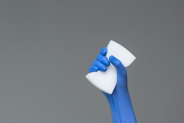 Рука в резиновой перчатке держит губку для мытья на сером