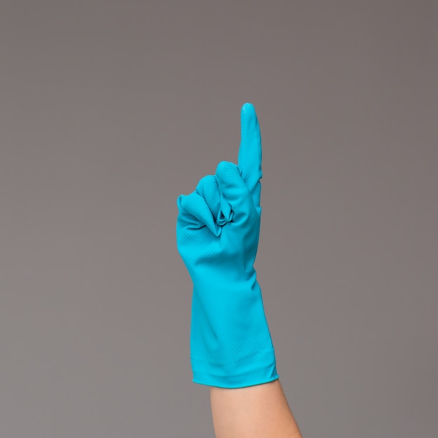 Hand in rubber glove points upwards with index finger. Neutral surface .