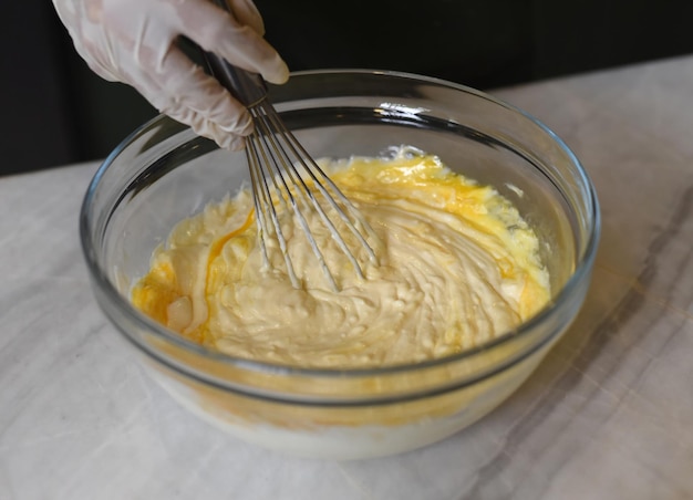 A hand in rubber glove stirring dough for a cake