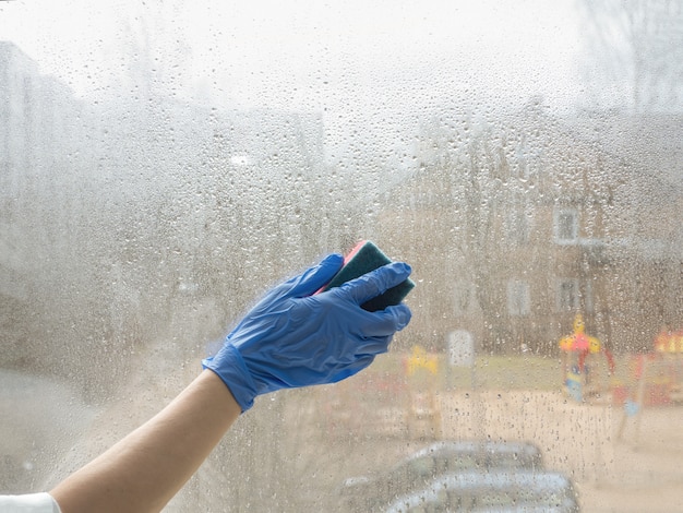 Hand in rubber gloves disinfects windows with disinfectant and sponge