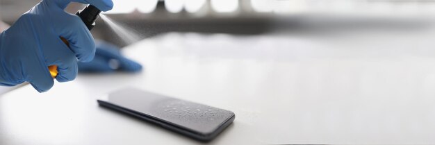 Hand in rubber gloves puffing antiseptic on phone screen closeup