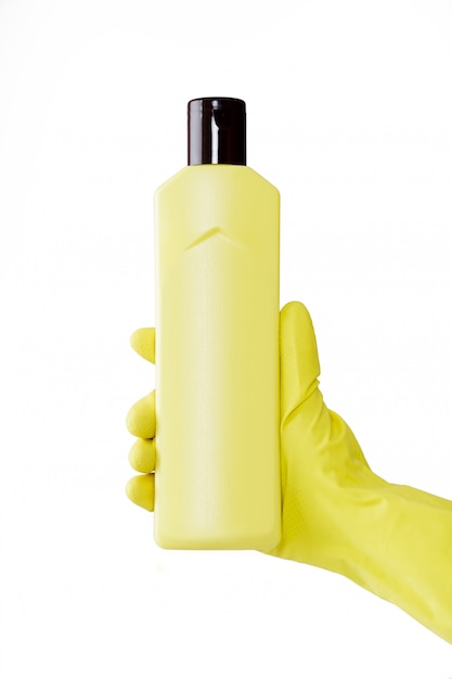 Hand in rubber yellow glove holds a bottle of liquid detergent on white background