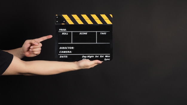 Foto mano che tiene e indica il ciak giallo e nero o l'uso di ardesia cinematografica nella produzione video e nell'industria cinematografica su sfondo nero.