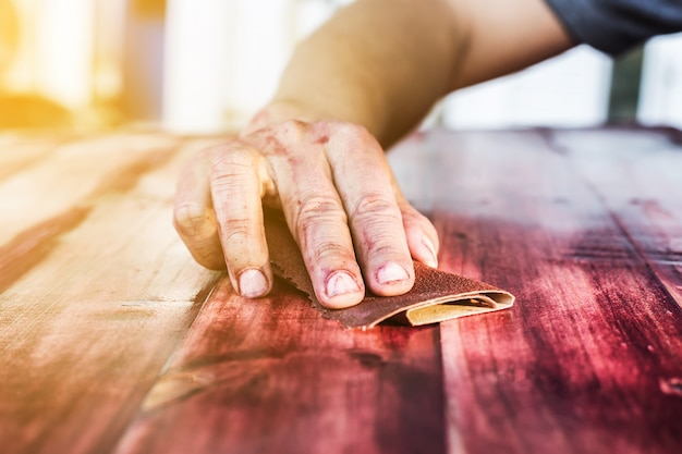 hand sanding and smoothing red wooden with sandpaper.