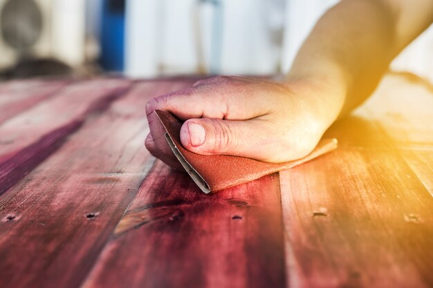 hand sanding and smoothing red wooden with sandpaper.