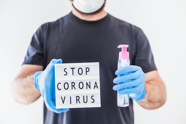 Photo hand sanitizer hygiene alcohol gel bottles and lightbox with text stop coronavirus in hands of man wearing latex medical gloves and protective mask during coronavirus covid-19 pandemics. healthcare