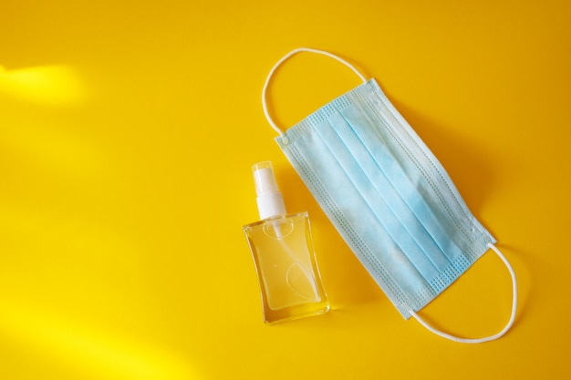 Hand sanitizer and medical protective mask on yellow table